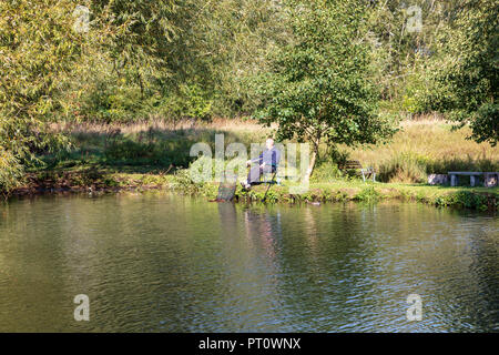 An angler relaxes by the side of the River Thames at Iffley in the warm autumn sunlight, Oxford, UK