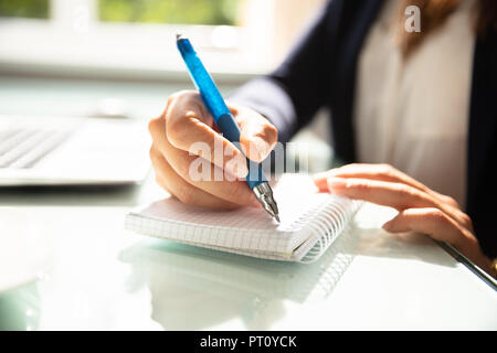 Close-up Of A Businesswoman's Hand Writing Note With Pen In Diary Over Desk Stock Photo