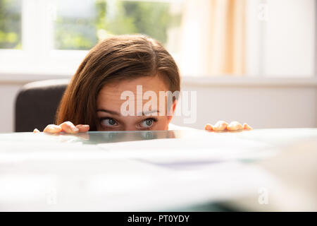 Afraid Businesswoman Peeking From The Edge Of Desk In Office Stock Photo