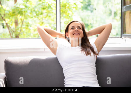 Smiling Young Woman Sitting On Sofa At Home Stock Photo
