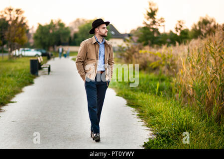 Handsome elegant man in the park wear jacket and fedora hat. Stock Photo