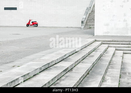 Lonely red scooter against white wall in background with plenty of urban environment in foreground
