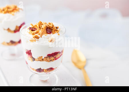 Close up of healthy raspberry yogurt parfait in a glass with golden spoon on white marble table over pink background with copy space. Stock Photo