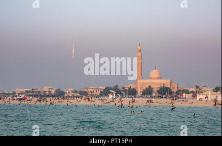 crowded beach in Dubai with Burj Khalifa reglecting a sunlight trhough the fog Stock Photo