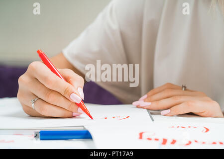 Calligrapher student practices in writing word LOVE with red marker on canvas. Creative artist freelancer working on project at home studio. Lettering Stock Photo