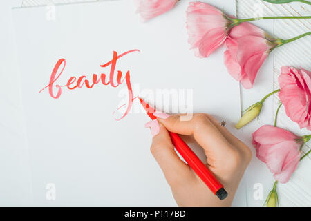 Closeup of calligrapher hands writes word beauty on white paper. Inscribing ornamental decorated letters. Calligraphy, graphic design, lettering, hand Stock Photo
