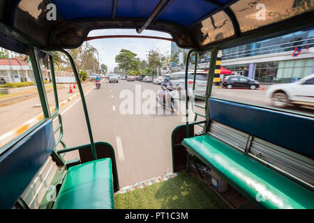 View of traffic on a street from the back of a songthaew (pick-up or small truck with benches along the sides) in Vientiane, Laos, on a sunny day. Stock Photo