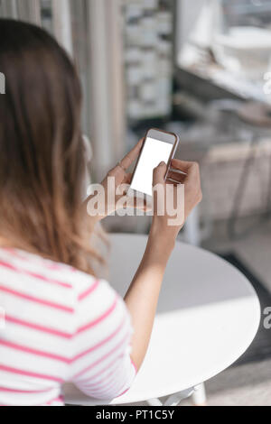 Young woman sitting in coffee shop, using smartphone Stock Photo