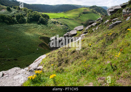 View down the steep slopes of a valley from high vantage point over rocky outcrops and fields and traditional stone walls. Stock Photo