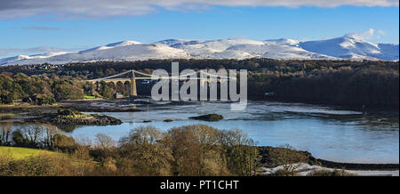 Menai Suspension Bridge designed by Thomas Telford viewed from Anglesey across the Menai Strait with snow capped hills in the background North Wales Stock Photo