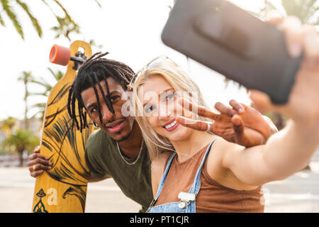 Portrait of multicultural young couple taking selfie with smartphone Stock Photo