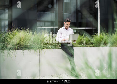 Smiling businessman using laptop outside office building Stock Photo