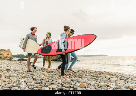 Happy friends with surfboards walking on stony beach Stock Photo