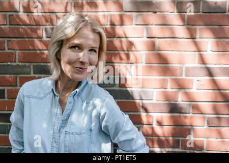 Portrait of smiling mature woman in front of brick wall Stock Photo