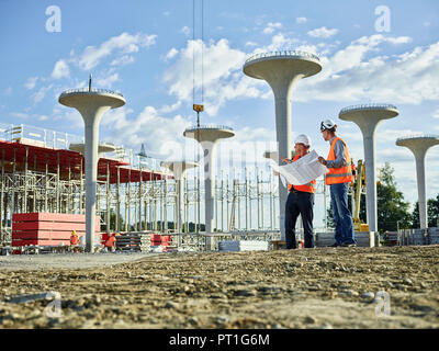 Workers on construction site looking at blueprint with the architect Stock Photo