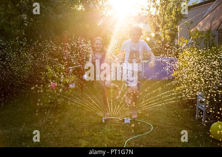 Brother and sister having fun with lawn sprinkler in the garden Stock Photo