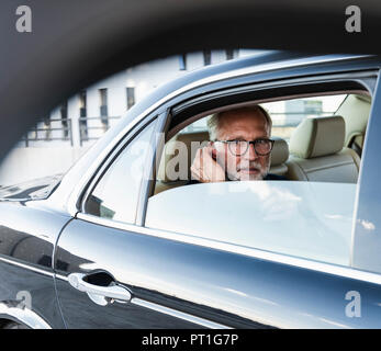 Mature businessman sitting on backseat in car, using earphones Stock Photo