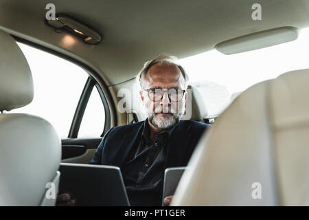 Mature businessman sitting on backseat in car, using digital tablet Stock Photo