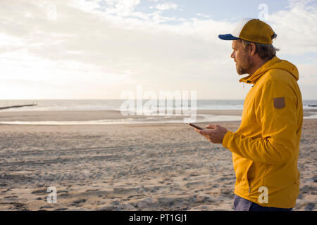 Man in yellow jacket, using smartphone on the beach Stock Photo