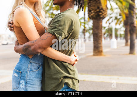 Spain, Barcelona, multicultural young couple embracing on promenade, partial view Stock Photo