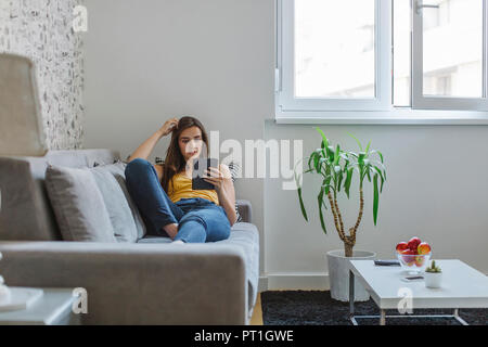 Woman on couch in the living room reading e-book Stock Photo