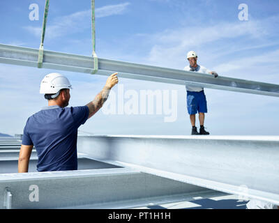 Worker on construction site standing on steel girder, getting instructions from lead worker Stock Photo
