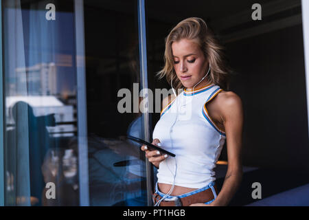 Woman in hotel room, using smartphone with earphones Stock Photo