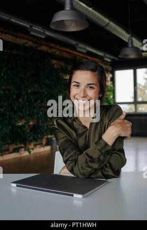 Portait of smiling young woman in office with laptop Stock Photo