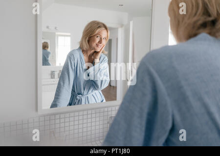 Portrait of smiling mature woman looking in bathroom mirror Stock Photo