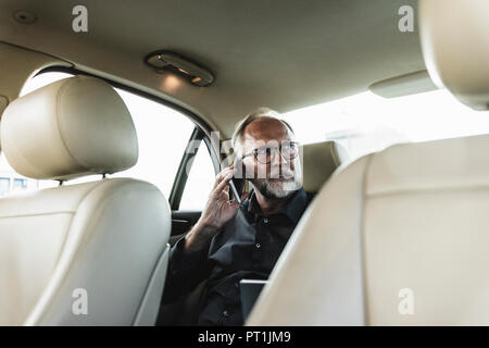 Mature businessman sitting on backseat in car, talking on the phone Stock Photo