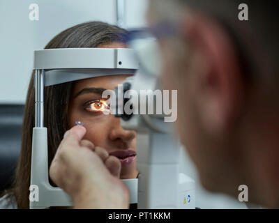 Optometrist examining young woman's eye, contact lens on index finger Stock Photo