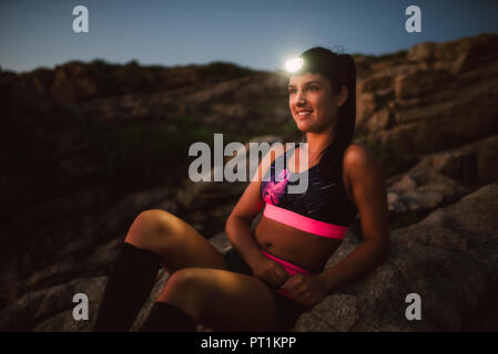 Sportive woman with headlamp sitting on rocks Stock Photo