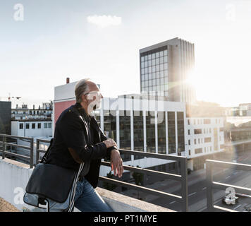 Mature man standing on rooftop, leaning on railing Stock Photo