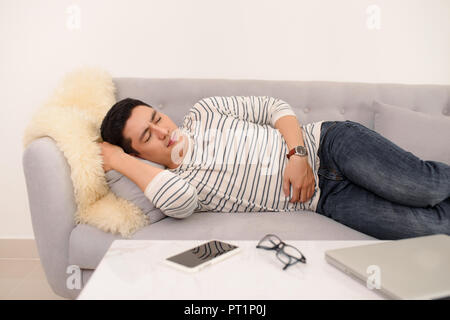 Handsome young man suffering from stomach ache while lying on sofa at home Stock Photo