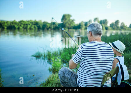Back view of grandfather and grandson fishing together at lakeshore Stock Photo