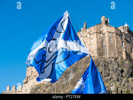 Holyrood, Edinburgh, Scotland, United Kingdom, 6th October 2018. All Under One Banner (AUOB) Scottish March and Rally for Independence, with supporters walking down the Royal Mile to Holyrood Park for a rally. AOUB is a pro-independence campaign for whose core aim is to march at regular intervals until Scotland achieves independence. Large Scottish Yes for Independence St Andrews Cross saltire flags waving in the wind below Edinburgh Castle Stock Photo