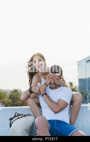 Laughing young woman surprising her boyfriend, covering his eyes Stock Photo