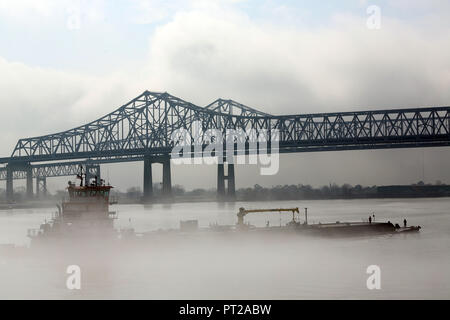 tug pushing barge under suspension bridge over foggy Mississippi River Stock Photo