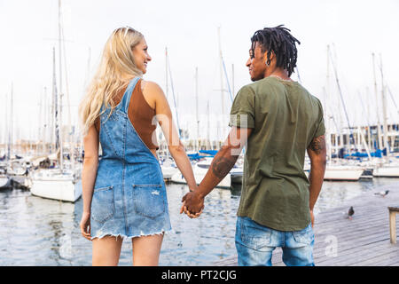 Back view of multicultural young couple standing hand in hand on jetty Stock Photo