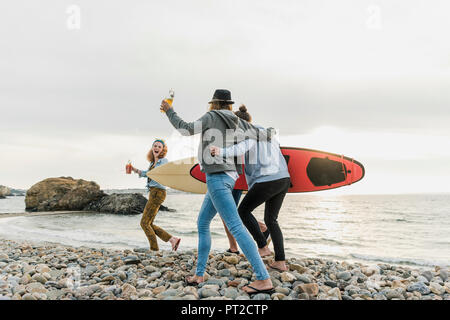 Happy friends with surfboards walking on stony beach Stock Photo