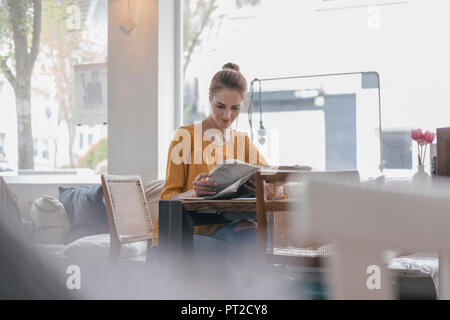 Young woman sitting in coworking space, reading newspaper Stock Photo