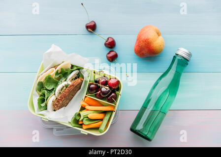 Healthy school food in a lunch box, vegetarian sandwich with cheese, lettuce, cucumber, egg and cress, sliced carrot and celery, cherries and pear Stock Photo