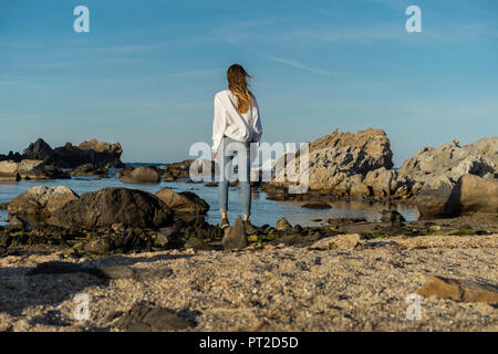 Woman looking sitting on rocks, looking at the sea Stock Photo
