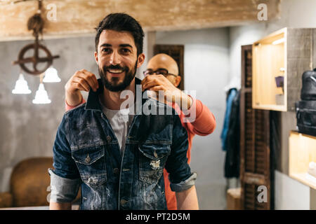 Handsome man trying on new denim jacket with stylist in modern boutique Stock Photo