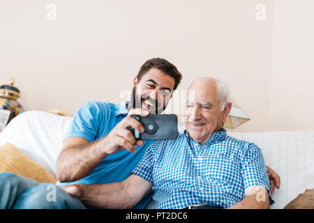 Portrait of adult grandson and his grandfather taking selfie with smartphone at home Stock Photo