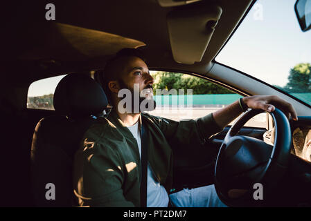 Bearded young man looking at rear-view mirror while driving car Stock Photo