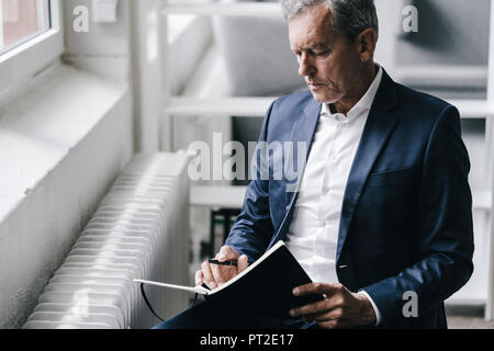 Pensive businessman with notebook sitting beside window Stock Photo