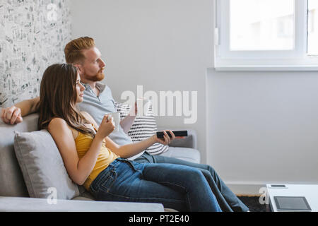 Couple sitting on couch drinking coffee and watching TV Stock Photo