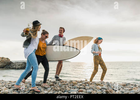 Happy friends with surfboards walking on stony beach Stock Photo