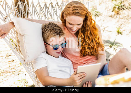 Happy mother and son lying in hammock looking at tablet Stock Photo